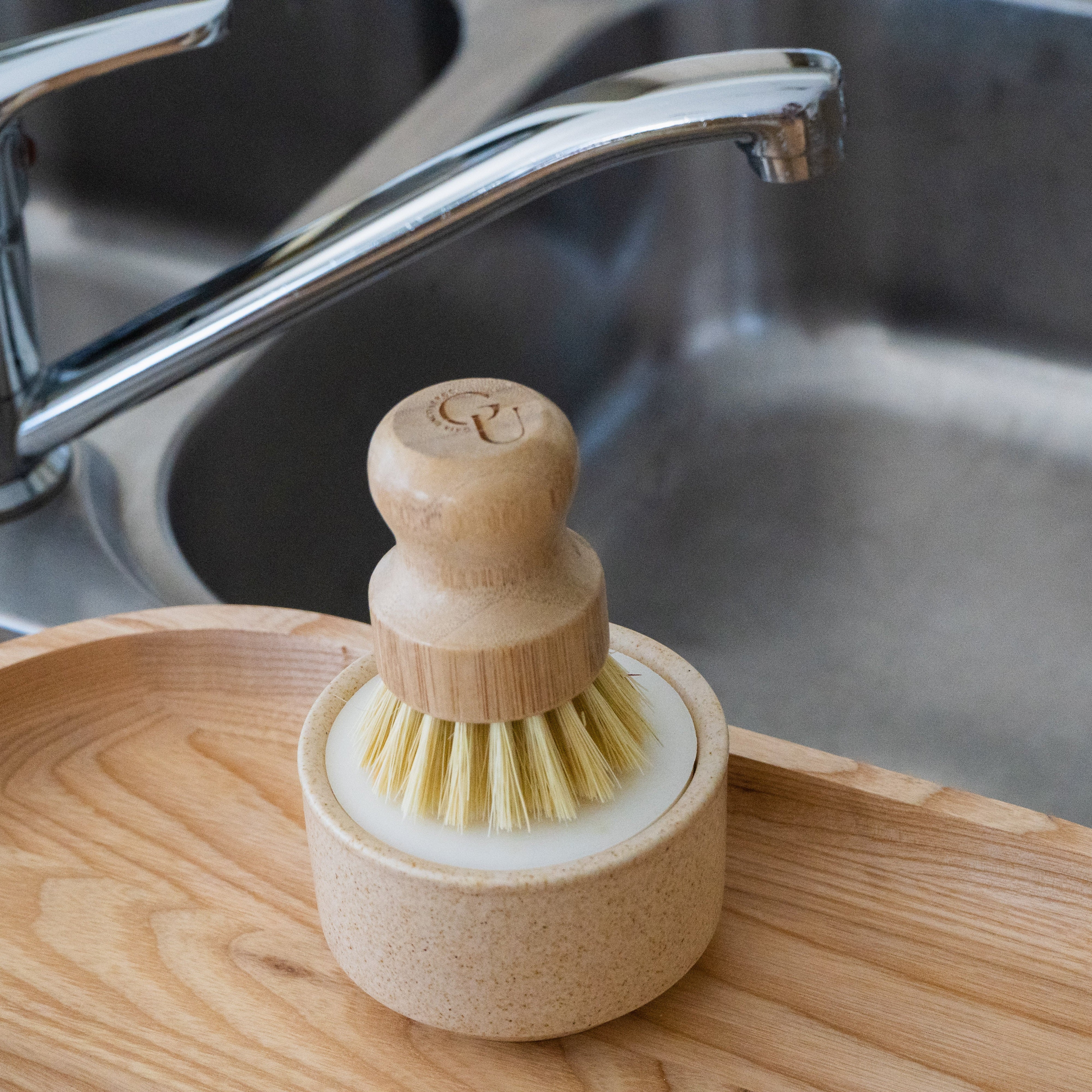 Wooden dish brush and soap holder on a wooden tray with a sink in the background